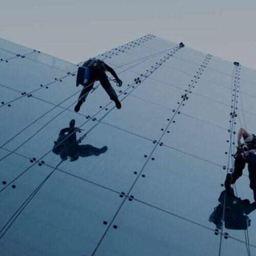 Imagen de dos trabajadores sujetadas a un arnes limpiando la fachada de un edificio